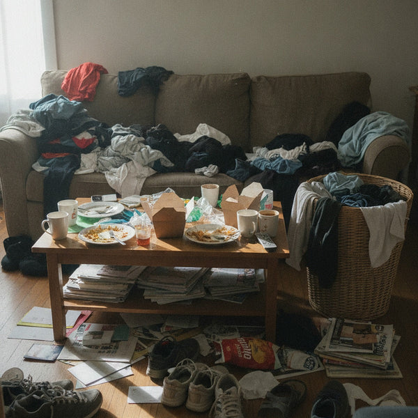 A living room with laundry, dishes and mail piled up