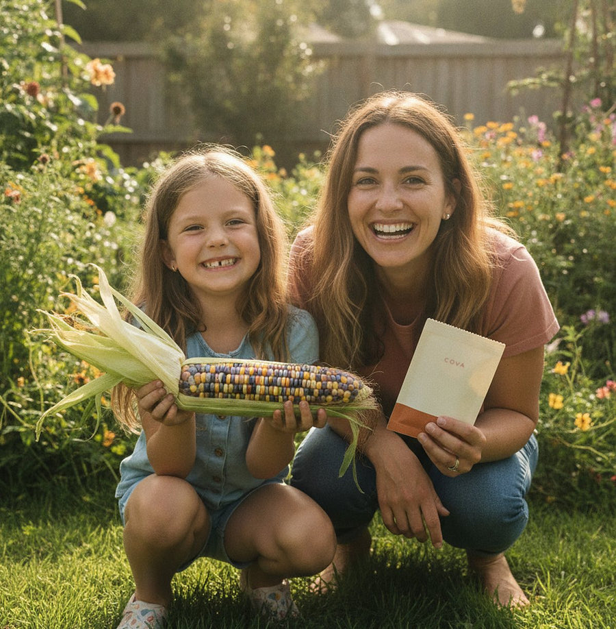 A mother and her daughter in a sunny garden holding glass gem corn and a COVA seed packet