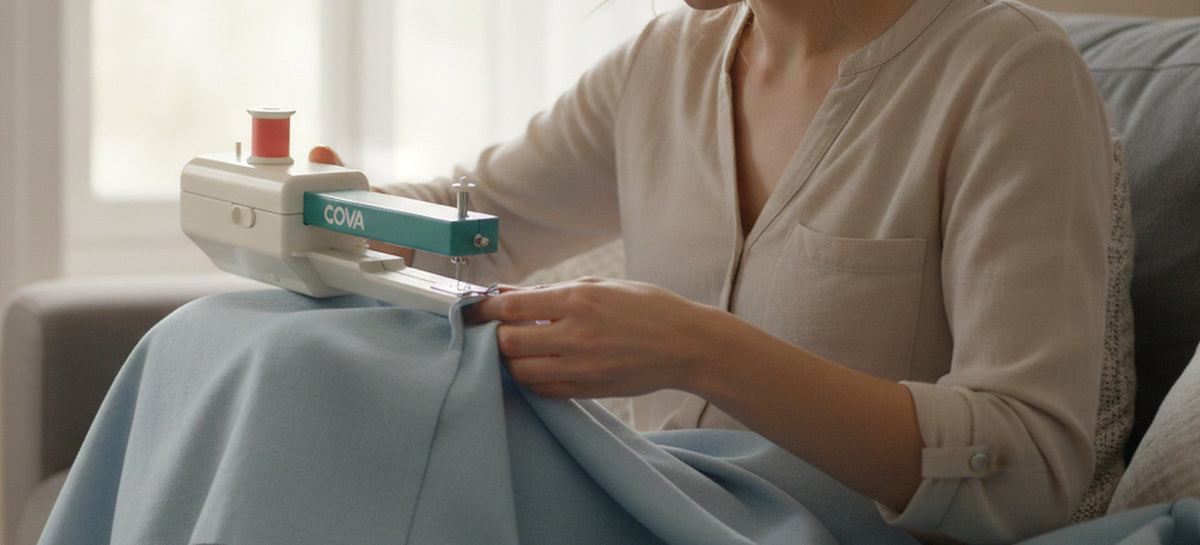 A woman hemming a curtain with the COVA handheld sewing machine on a sofa by a window