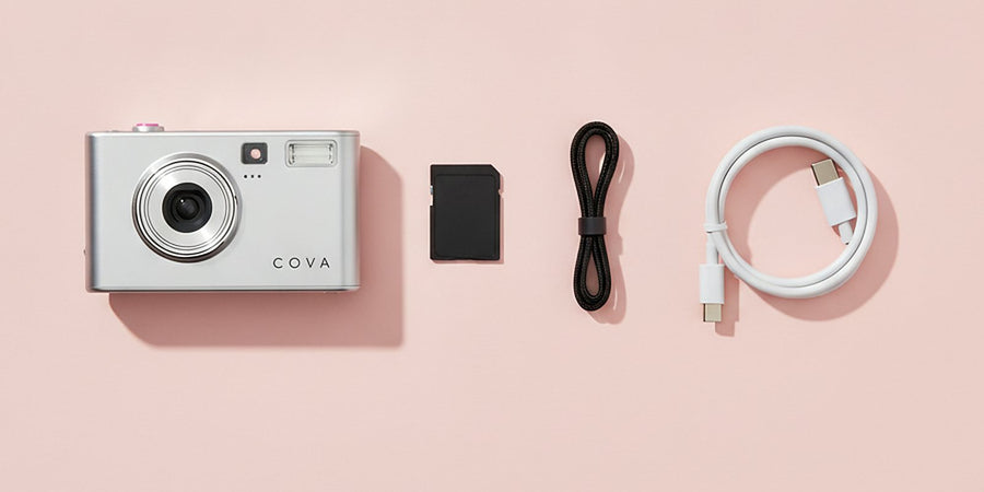 The COVA camera, memory card, wrist strap and cable laid out on pink paper